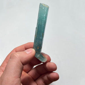 Hand holding a clear, ribbed Aquamarine crystal object against a white background