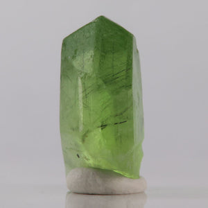 Green peridot crystal on a white base against a gray background