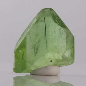 Green peridot crystal on a white stand against a gray background