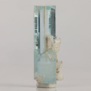 Pakistani aquamarine crystal with small dark inclusions, subtle blue color zoning, and attached white mineral deposits.