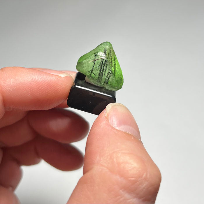 Green Peridot crystal on a reflective surface with a gray background