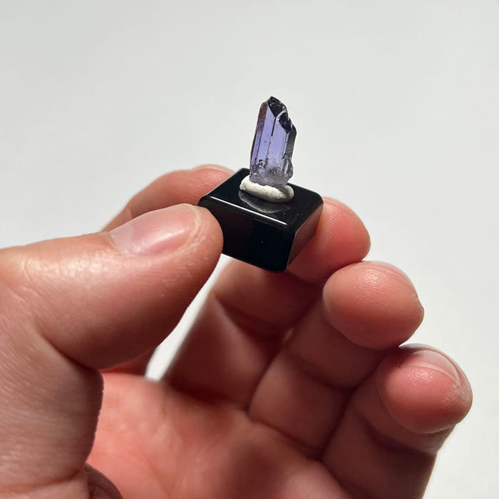 Tanzanite Crystal with purple and blue hues on a white base against a gray background