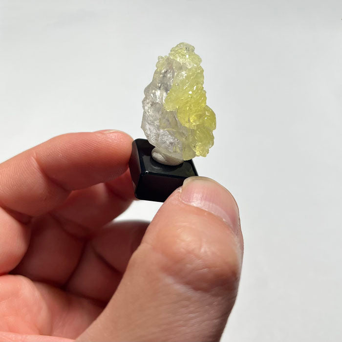 Hand holding a small crystal or mineral sample on a white background