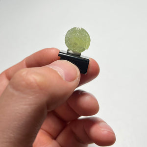 Hand holding a small round prehnite crystal object with a white background