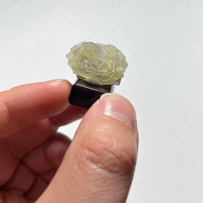 Prehnite Crystal flower rock on a white stand with a gray background