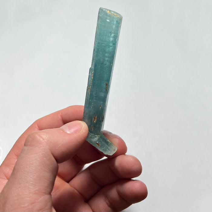 Hand holding a clear, ribbed Aquamarine crystal object against a white background