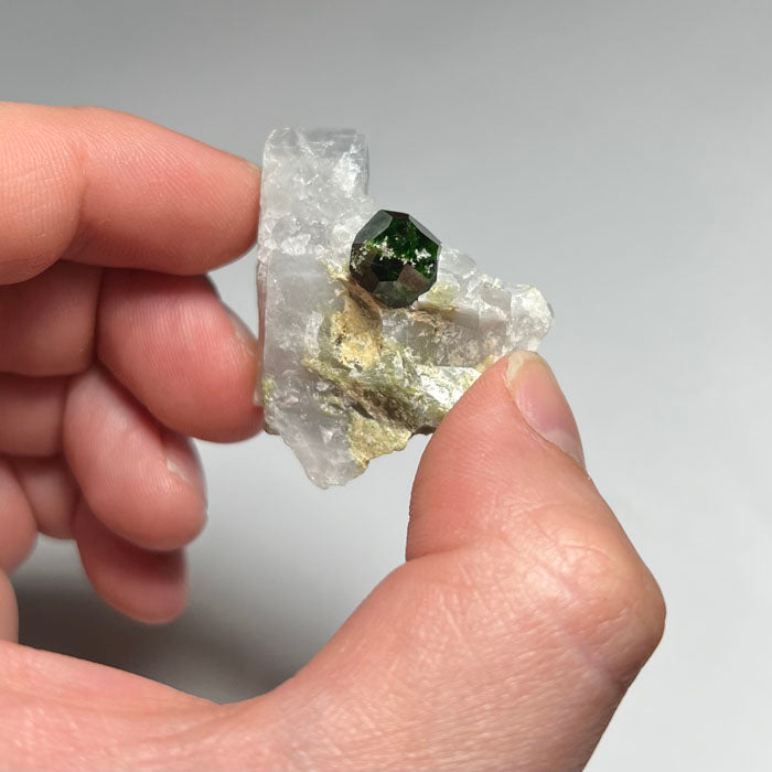 Mineral sample with a green demnatoid garnet crystal on a white background