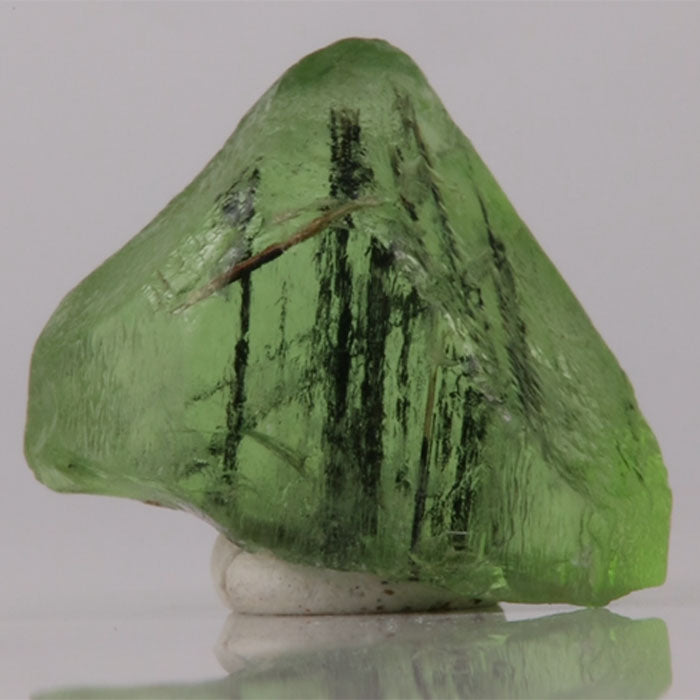Green Peridot crystal on a reflective surface with a gray background