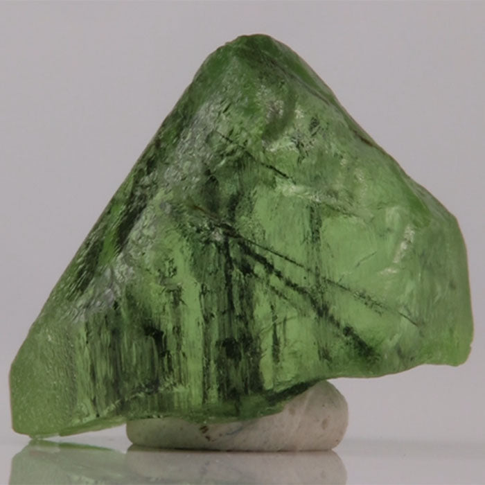 Green Peridot mineral crystal on a reflective surface with a gray background