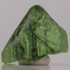 Green Peridot mineral crystal on a reflective surface with a gray background