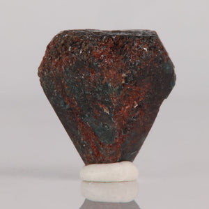 Raw Alexandrite stone on a white stand against a gray background