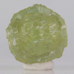Green prehnite crystal sphere on a white base against a gray background