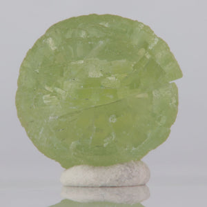 Green Prehnite stone on a white pedestal against a gray background