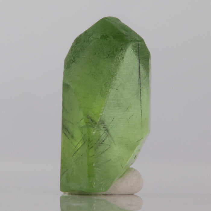 Green peridot crystal on a reflective surface with a gray background