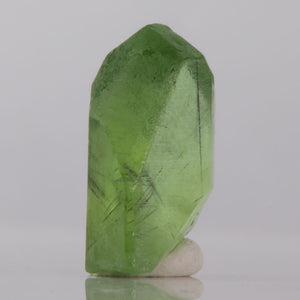 Green peridot crystal on a reflective surface with a gray background
