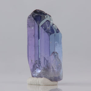 Tanzanite Crystal with purple and blue hues on a white base against a gray background