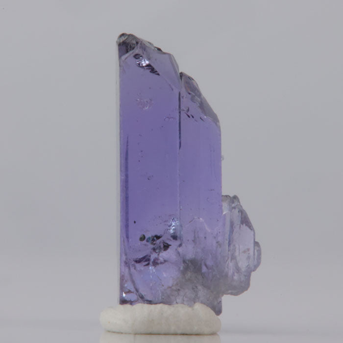 Purple tanzanite crystal on a white base against a gray background