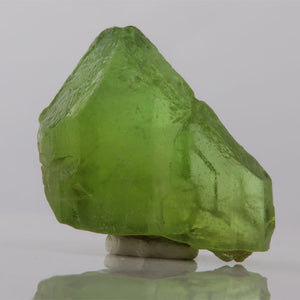 Green crystal on a reflective surface with a gray background