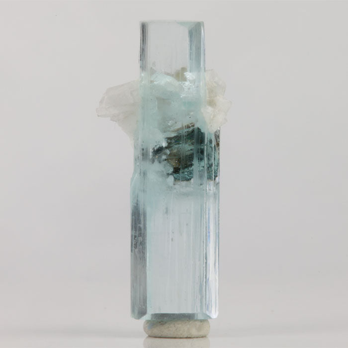 Double-terminated aquamarine crystal from Shigar Mine Pakistan with a dark mineral crystal surrounded by white matrix.