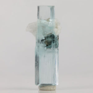 Double-terminated aquamarine crystal from Shigar Mine Pakistan with a dark mineral crystal surrounded by white matrix.