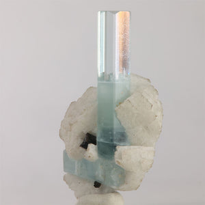 Reverse view of icy-blue aquamarine with smaller associated blue crystal, white matrix, and dark mineral inclusions.