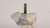 Natural tourmaline thumbnail specimen featuring a slender green crystal standing vertically above a light-colored mineral base.