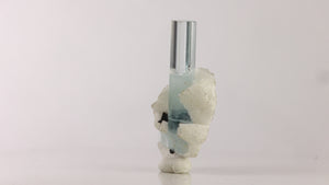 Reverse view of icy-blue aquamarine with smaller associated blue crystal, white matrix, and dark mineral inclusions.
