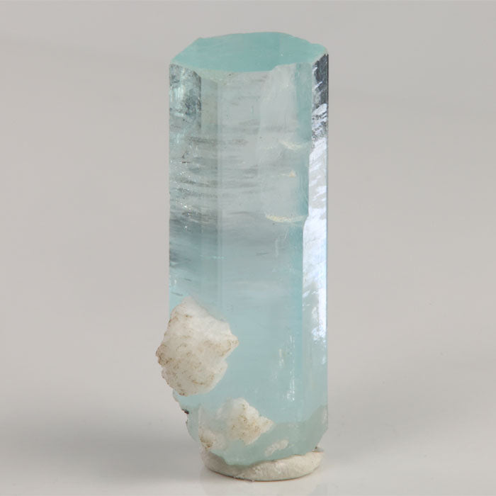 Upright icy-blue aquamarine crystal from Shigar Mine Pakistan with a broad natural hexagonal termination and attached white matrix.