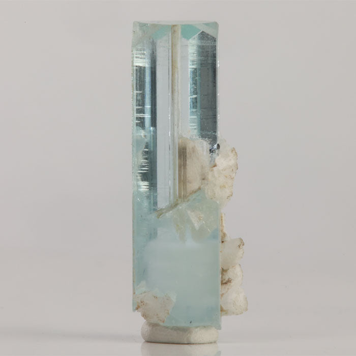 Pakistani aquamarine crystal with small dark inclusions, subtle blue color zoning, and attached white mineral deposits.
