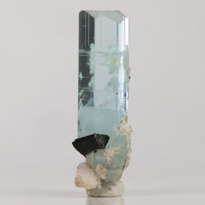 Aquamarine specimen with prominent black mineral inclusion near the base and delicate blue coloration.