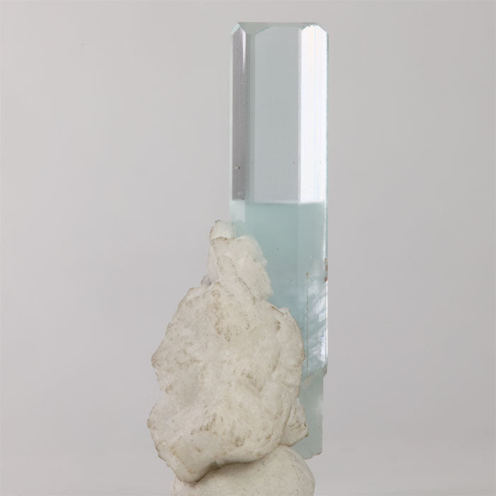 Side view of aquamarine crystal showing transparent upper faces and attached white mineral matrix.