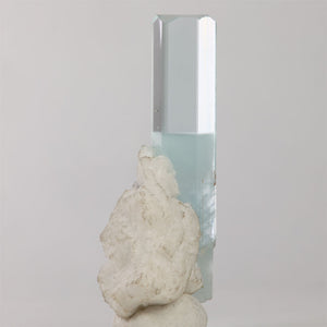 Side view of aquamarine crystal showing transparent upper faces and attached white mineral matrix.